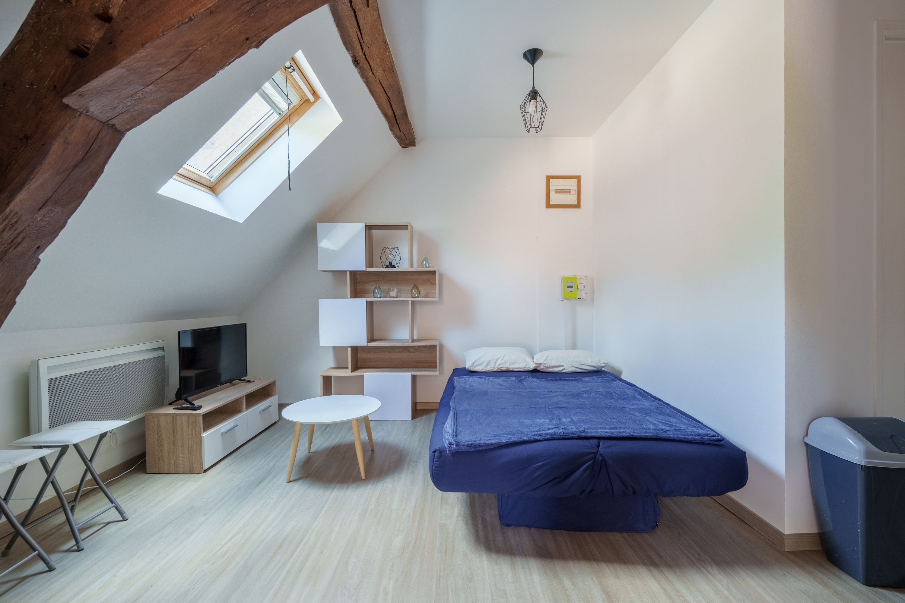 Un dormitorio moderno con techo inclinado, una cama, un televisor y estanterías empotradas.