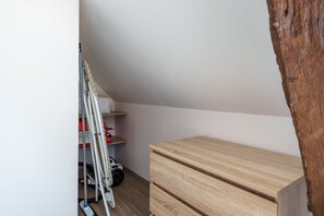 A room with a wooden dresser, a vacuum cleaner, and a drying rack against a white wall. - Le 3 Saint-Blaise - Joli studio à Autun (Autun)