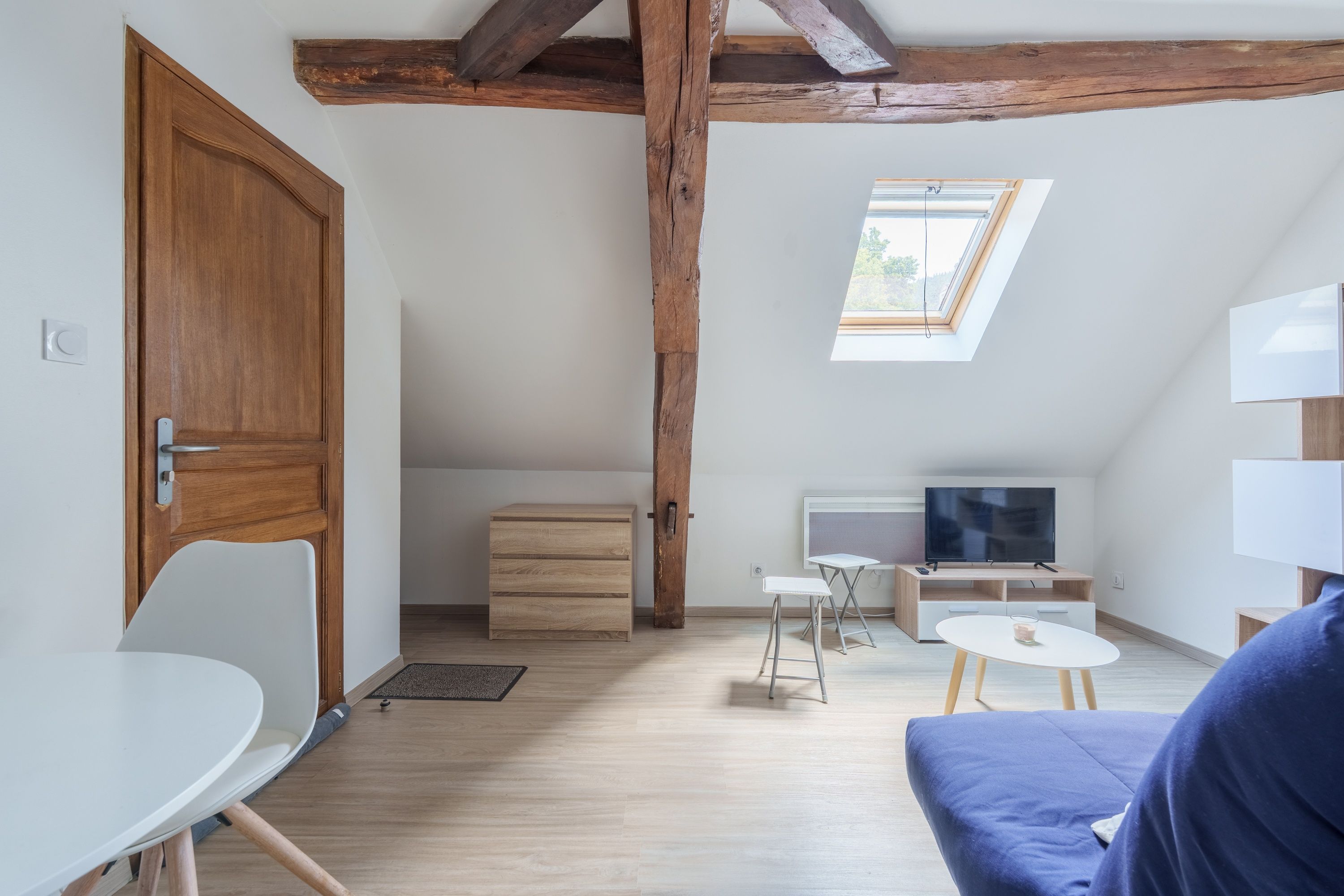 A modern, well-lit room with a wooden ceiling, a television, a small table, and a sofa.