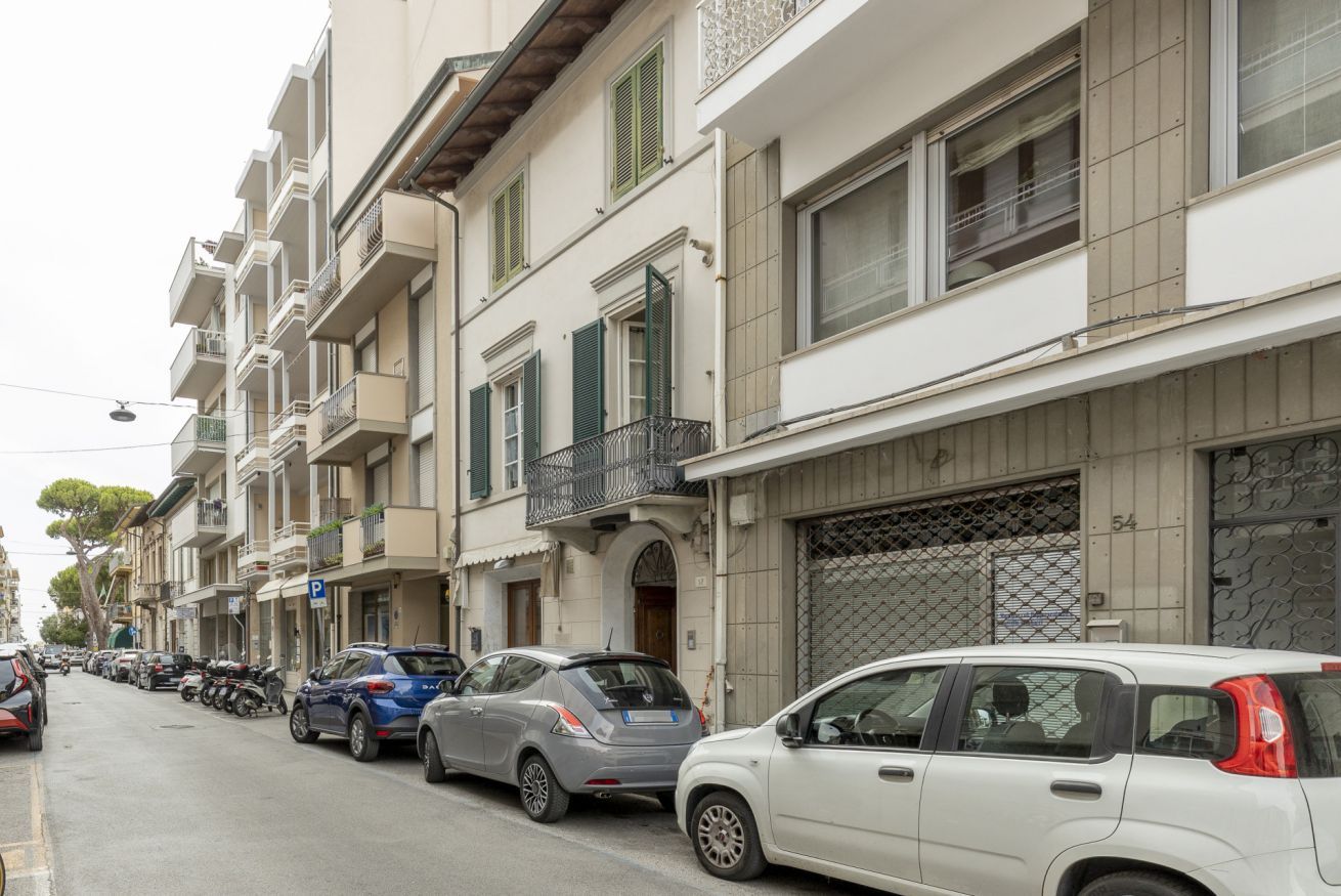 A street lined with multi-story buildings, parked cars, and a clear sky.