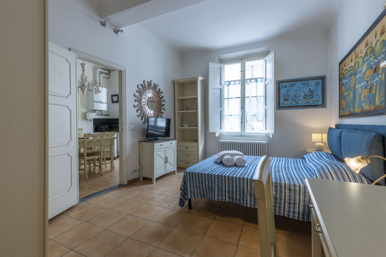 A bedroom with a bed, a desk, a chair, a television, a window, and a radiator.