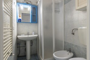Ein Badezimmer mit einem Waschbecken auf Säule, einem Spiegel, einer Duschkabine und einer Toilette.