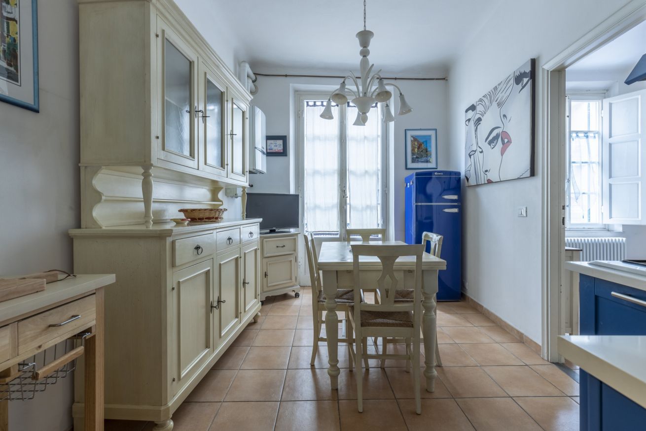 Une cuisine avec des meubles blancs, une table à manger avec des chaises et un réfrigérateur bleu.