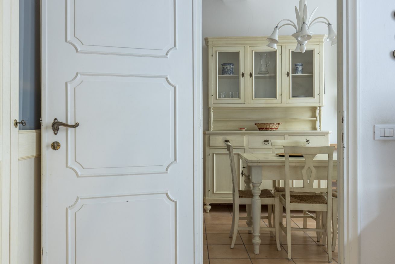 Une porte blanche avec une poignée en laiton, une table blanche avec des chaises et un buffet de couleur crème doté de portes en verre.