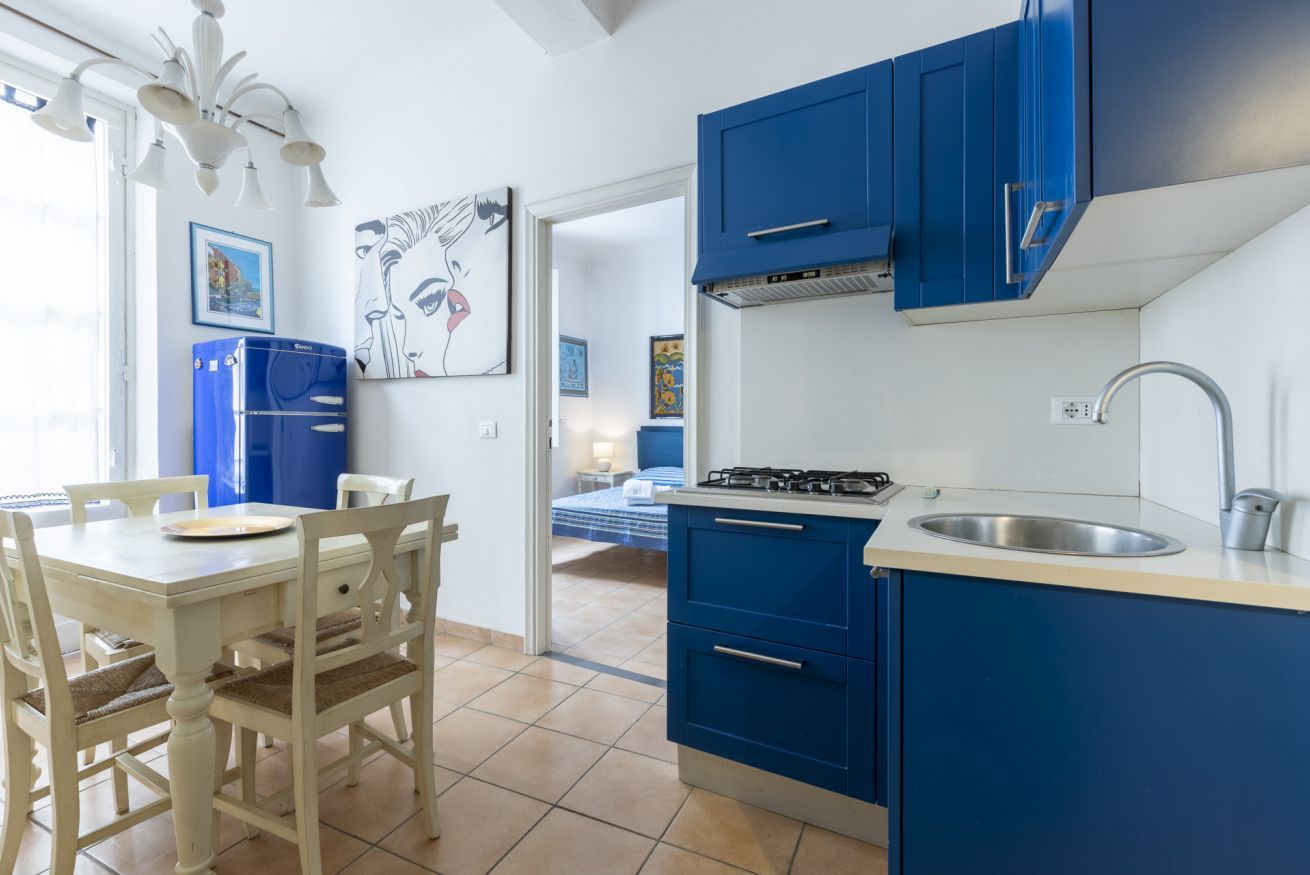 A compact kitchen with blue cabinets, a white countertop, and a dining area with a table and chairs.