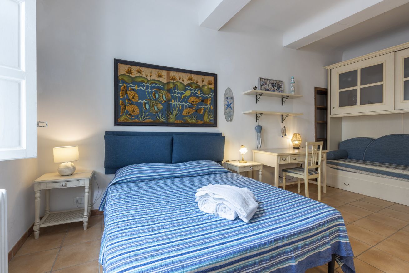 A bedroom with a bed, a desk, a chair, a nightstand, a wall painting, and a cabinet.