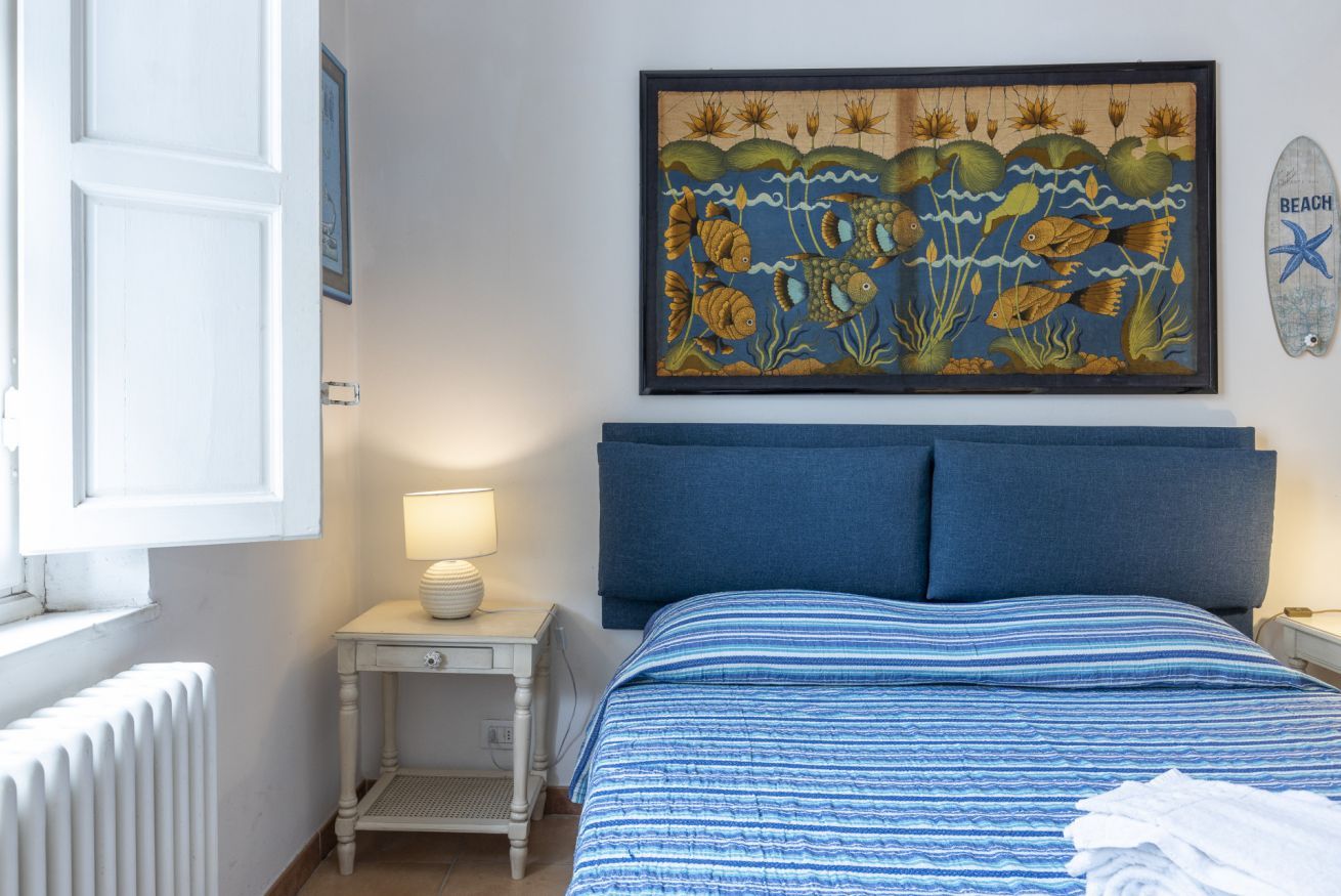 Une chambre à coucher comprenant un lit, une table de chevet, une lampe, un radiateur, une œuvre d’art encadrée et une plaque décorative fixée au mur.