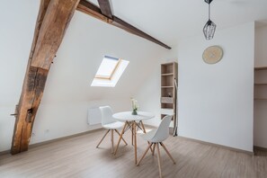 A room with a sloped ceiling, a skylight, a round table with chairs, a bookshelf, and a wall clock. - Le 4 Saint-Blaise - Studio spacieux et rénové (Autun)