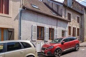 A two-story building with a stone facade, a red car parked in front, and a beige car parked to the left. - Le 4 Saint-Blaise - Studio spacieux et rénové (Autun)