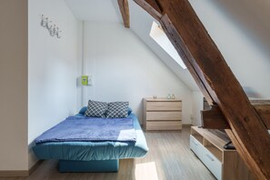 Un dormitorio con techo inclinado, una cama con colcha azul, una mesita de noche con lámpara y un aparador de madera.