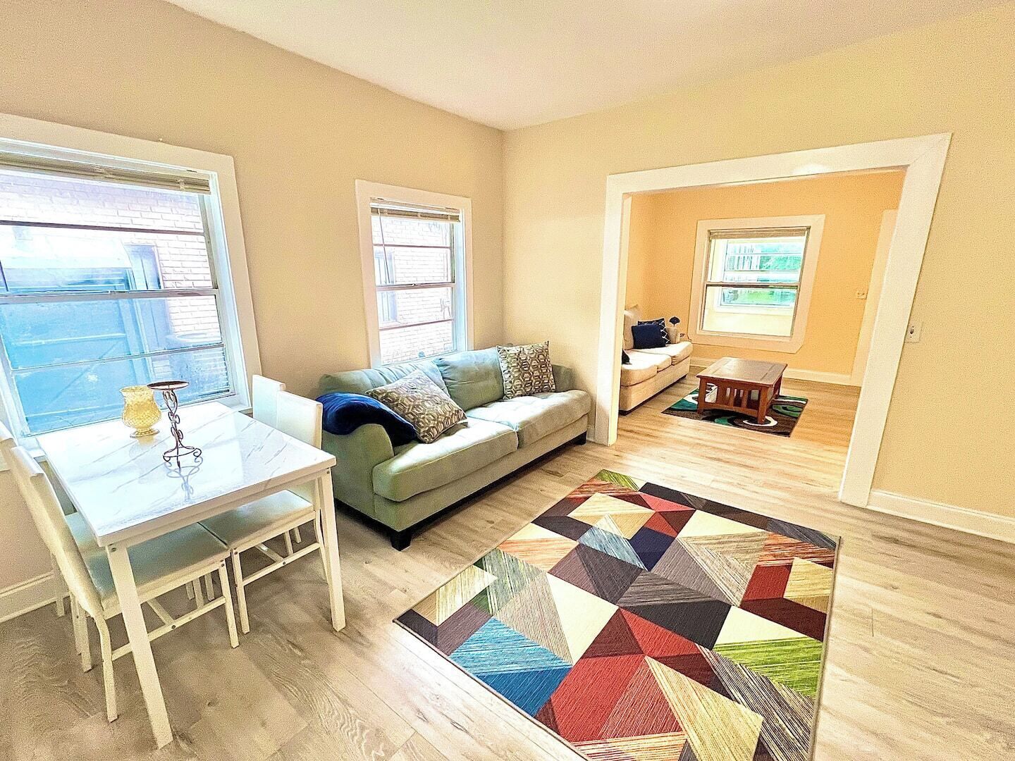 A living room with a sofa, a coffee table, a dining table with chairs, and a colorful rug.