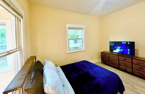 A bedroom with a bed, a dresser, a television, and a window. - The Blue~nicorn Bungalow - 7 mins to DT (Jacksonville)