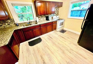 A kitchen with wooden cabinets, a granite countertop, a stove, and a refrigerator. - The Blue~nicorn Bungalow - 7 mins to DT (Jacksonville)