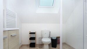 Une petite salle de bain propre, équipée de toilettes, d’une étagère et d’un espace douche.