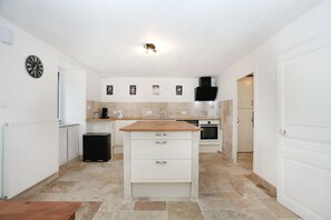 A modern kitchen with white cabinetry, a central island, a built-in oven, and a black range hood. - Le Refuge de Brocéliande - Près des sentiers (Beignon)