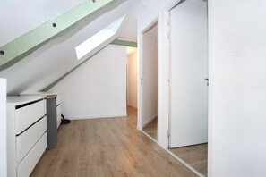 A room with a sloped ceiling, wooden flooring, a white wardrobe, and a door leading to another room. - Le Refuge de Brocéliande - Près des sentiers (Beignon)