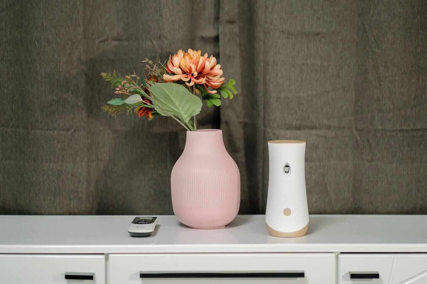 Uma escrivaninha com um vaso rosa com flores, um vaso branco e um controle remoto.
