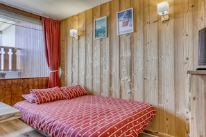 A room with a wooden wall, a bed with red bedding, and two posters. - L’Écrin du Cernix - 400m du télésiège (Cohennoz)