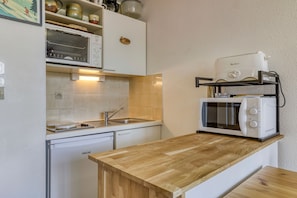 A compact kitchen with white cabinetry, a built-in microwave, a toaster, and a sink. - L’Écrin du Cernix - 400m du télésiège (Cohennoz)