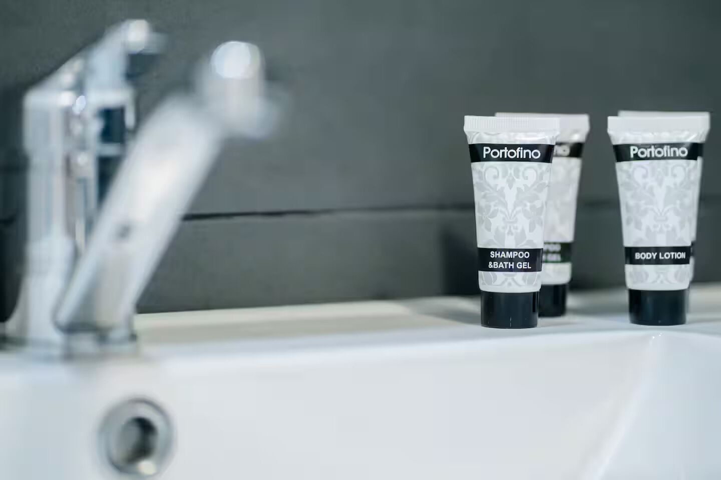 Zwei Portofino Pflegeprodukte, eines mit der Aufschrift Shampoo und Duschgel, das andere als Körperlotion, auf einem Badezimmerwaschbecken platziert.