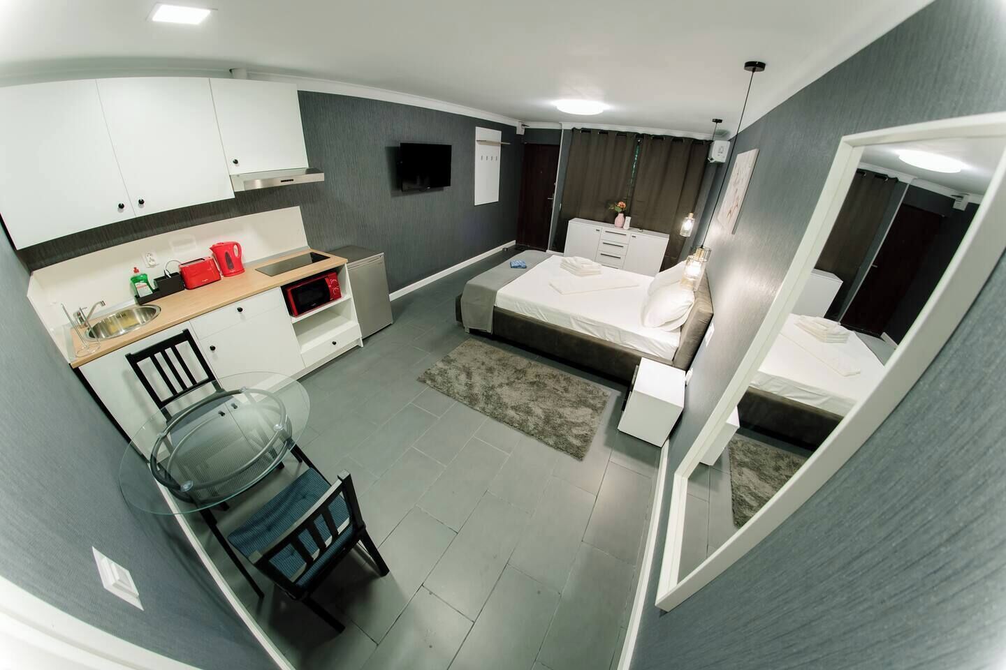 A compact hotel room with a kitchenette, a bed, a seating area, and a bathroom.