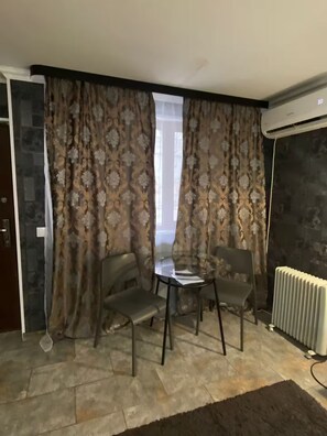Une pièce avec une table en verre, deux chaises, des rideaux à motifs, un radiateur et un mur en pierre.