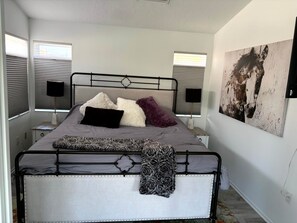 Ein Bett mit Metallgestell, mehreren Kissen, einer Decke, Nachttischlampen und einem Wandbild.