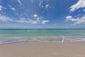 Ein Strand mit klarem türkisfarbenem Wasser und einem Sandufer unter blauem Himmel mit vereinzelten Wolken.