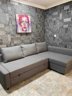 A grey sectional sofa with a storage drawer, positioned against a wall with a textured, dark grey tile pattern.