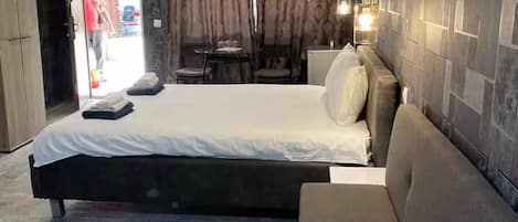 A modern bedroom with a bed, a sofa, a dining area, and a bathroom.