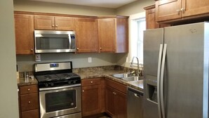A kitchen with wooden cabinets, a stainless steel refrigerator, a microwave, a stove, and a sink. - Modern Townhome Walking Distance of Downtown (Houghton)