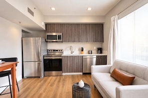 A compact kitchenette with a microwave, stove, and refrigerator, a dining area with a table and chairs, and a seating area with a sofa and a decorative vase. - The Penn Hotel - Sleeps 3 & Gaslamp Nightlife Now! (San Diego)