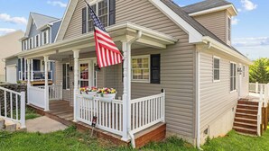 Une maison à deux étages avec un porche, un drapeau et des pots de fleurs.