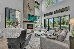 A modern living room with a fireplace, comfortable seating, and large windows offering a view of the outdoors. - Modern Mountain Luxury Lodge! Golf Access & Amenities! (Truckee)