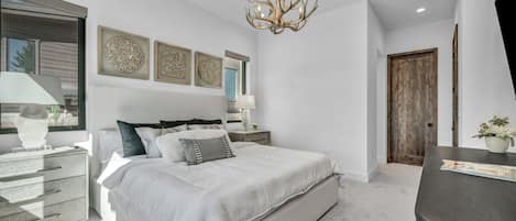 Une chambre à coucher moderne avec un grand lit, des tables de chevet, un lustre et des œuvres d’art accrochées aux murs.