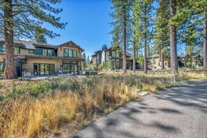 A modern residential area with multiple houses, a paved driveway, and surrounding tall pine trees. - Modern Mountain Luxury Lodge! Golf Access & Amenities! (Truckee)