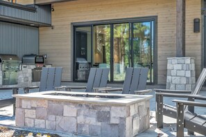 Ein Außenbereich mit Steinkamin, Metallstühlen, Grill und einer Schiebetür zu einer überdachten Terrasse.