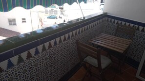 Un balcón con baldosas estampadas, un banco de madera y una silla.