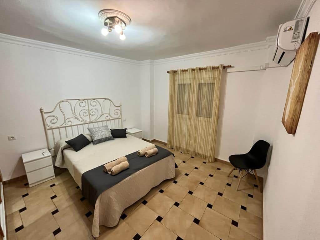 A bedroom with a bed, a chair, a nightstand, and a ceiling light fixture.