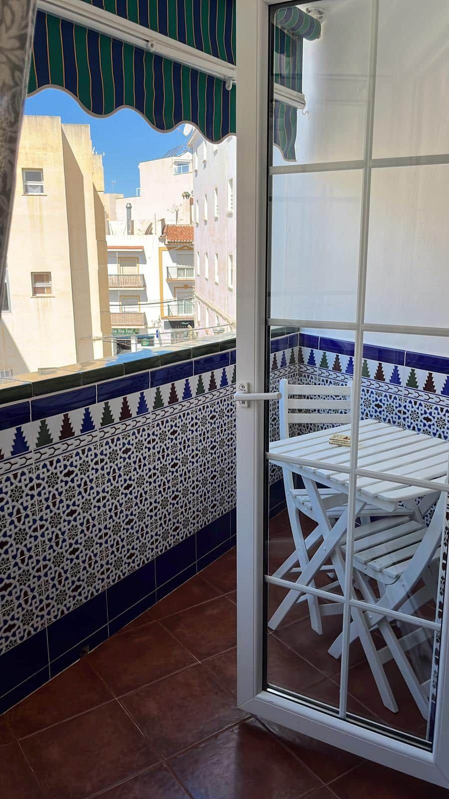 A balcony with a white table and chairs, patterned tiles, and a view of buildings.