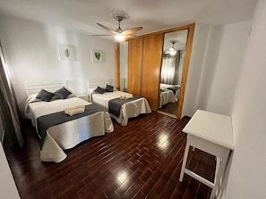 Ein Zimmer mit zwei Betten, einem Deckenventilator, einem kleinen Tisch und einem Spiegel.
