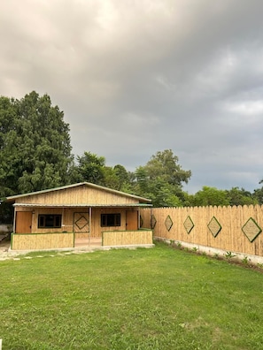 Una casa de fusta de planta baixa amb un pati tancat per una valla, envoltada d'arbres.