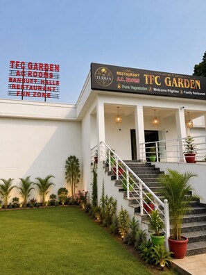 A building with a sign for TFC Garden, featuring a staircase, potted plants, and a well-maintained lawn.