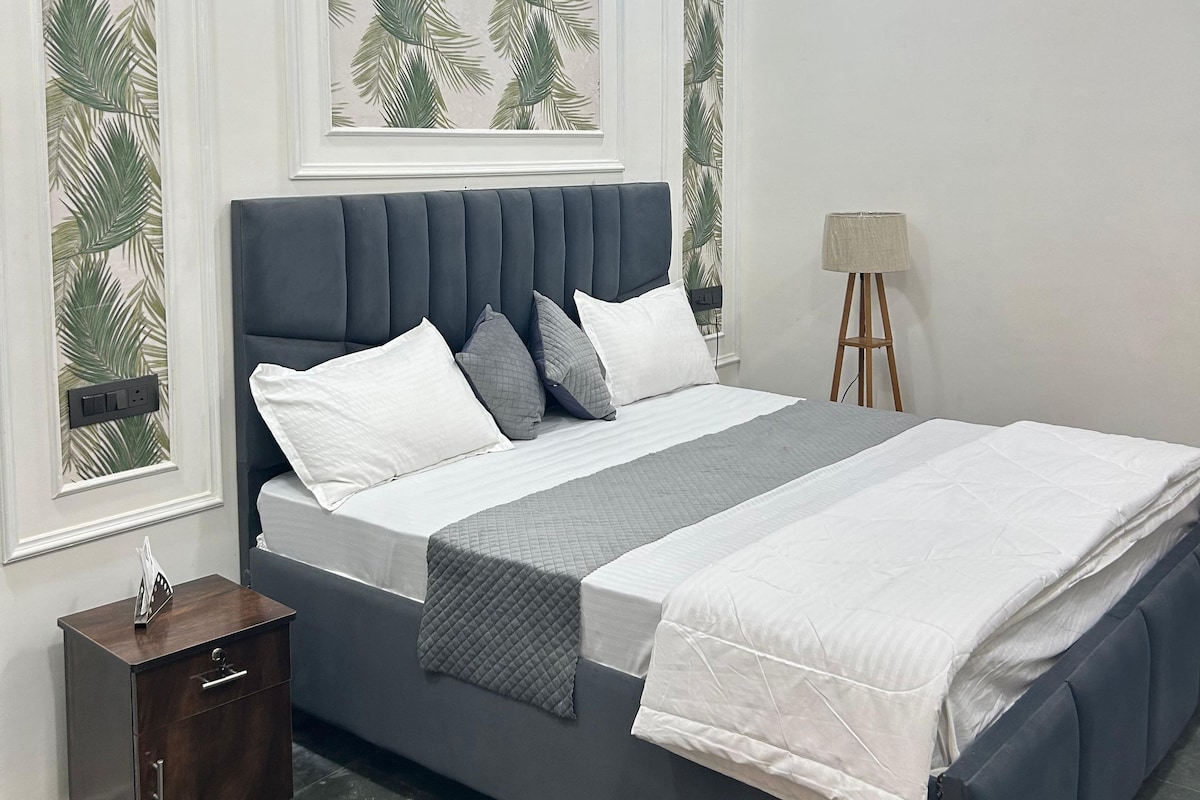 A bedroom with a bed, a nightstand, a lamp, and an air conditioning unit.
