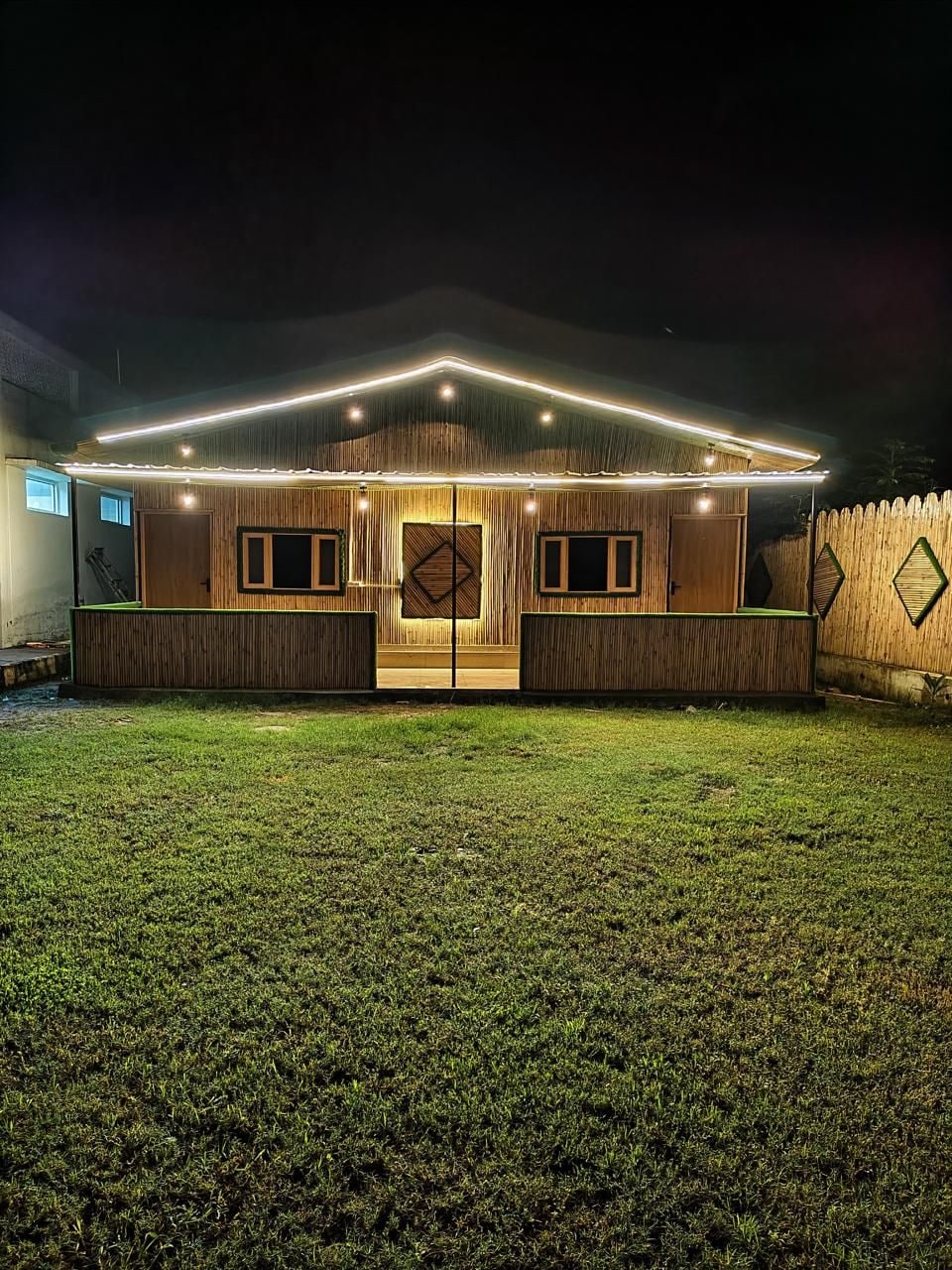 Una casa con porche delantero, dos puertas y un patio cercado de noche.