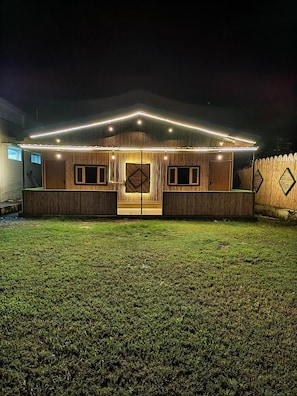 A house with a front porch, two doors, and a fenced yard at night.