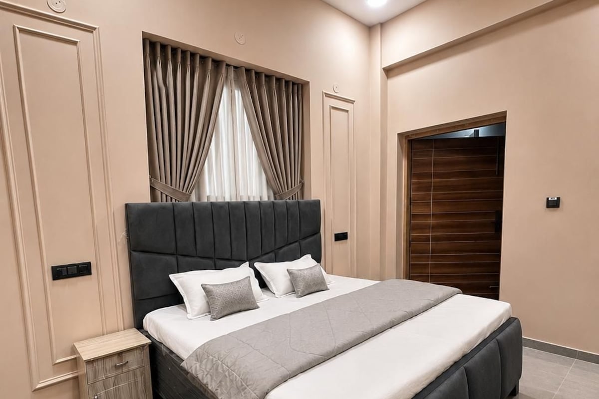 A modern bedroom with a large bed, a bedside table, a wardrobe, and a ceiling fan.