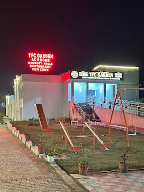 A building with a sign for TFC Garden, featuring a ramp, a slide, and a swing set.