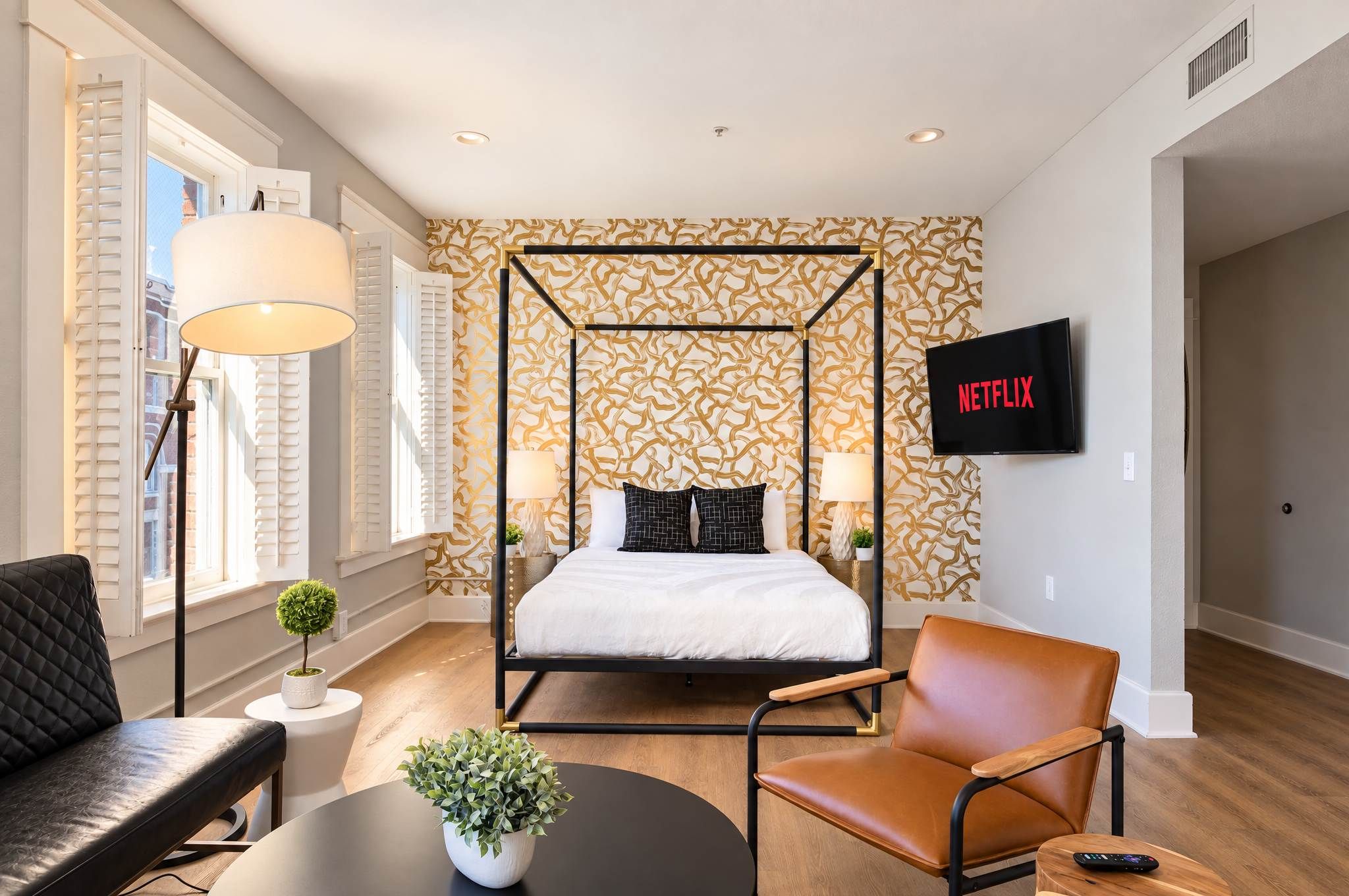 Un dormitorio moderno con cama con dosel, televisión y zona de estar con una silla y mesa.