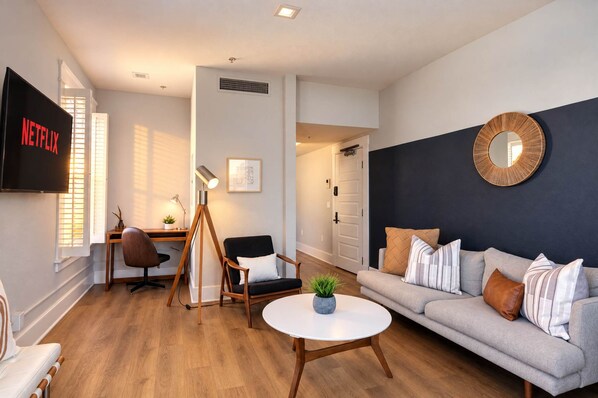 🛋 Expansive living room—featuring a plush sofa lounge, smart TV, and warm hardwood flooring. - The Penn Hotel - Smart TV, King Bed & Walkability! (San Diego)